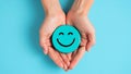 Hands gently holding cheerful smiling face button on light blue background Royalty Free Stock Photo