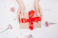 Hands of girl holding present gift craft box with red bow on white background with flowers, flat lay. Concept mother day Royalty Free Stock Photo