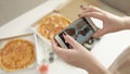 Hands of girl with smartphone taking picture of delicious pizza