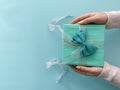 Hands giving blue present with big bow. Top view of gift box over pastel blue background Royalty Free Stock Photo