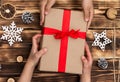 Hands giving or receiving a gift in craft paper with a red ribbon on wood Christmas and New Year background. Top view Royalty Free Stock Photo