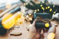 Hands giving rustic christmas gift in black wrapping paper with cinnamon decoration on background of golden lights, pine branches Royalty Free Stock Photo