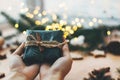 Hands giving rustic christmas gift in black wrapping paper with cinnamon decoration on background of golden lights, pine branches Royalty Free Stock Photo