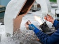 The hands of a glassblower woman holding a glass rod over the flame of a burner against the background of the workplace