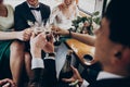 Hands with glasses of champagne clinking, stylish happy bride and groom toasting laughing and having fun with bridesmaids and