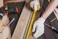 Hands in gloves of joiner in carpentry. Carpenter is measuring length of wood planks or timbers by measuring tape or ruler.