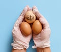 Hands in gloves keeping eggs with inscription EASTER over blue background Royalty Free Stock Photo