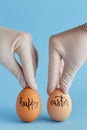 Hands in gloves keeping eggs with inscription HAPPY EASTER over blue background Royalty Free Stock Photo