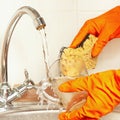 Hands in gloves with sponge wash glass under running water