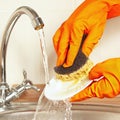 Hands in gloves with sponge wash the plate under running water in kitchen Royalty Free Stock Photo