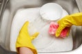 Hands in gloves washing drinking glass with pink cleaning sponge Royalty Free Stock Photo
