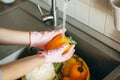 Hands in gloves washing pepper under water stream in sink during virus epidemic. Washing vegetables. Woman in pink hands cleaning Royalty Free Stock Photo