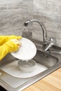 Hands in gloves washing white plate against kitchen sink Royalty Free Stock Photo