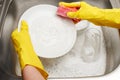 Hands in gloves washing white plate with pink cleaning sponge Royalty Free Stock Photo