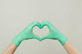 Hands in green doctor gloves making heart on gray background