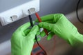 Hands in green gloves plug voltmeter into an outlet in wall