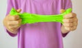 Hands with green slime close up. A child in a purple t-shirt stretching slime. Trendy liquid toy sticks to hands. kids