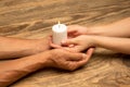 Hands guarding, holding a white candle on wooden background with copyspace