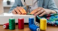 Hands guiding a print fabric through a white electric sewing machine needle with colorful thread spools in the foreground. Royalty Free Stock Photo