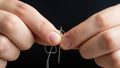 Hands guiding a white thread into the eye of a needle on a black background. Royalty Free Stock Photo