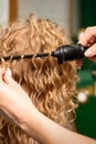 Hands of hairstylist curl wavy hair of young woman using a curling iron for hair curls in the beauty salon rear view. Royalty Free Stock Photo