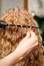 Hands of hairstylist curl wavy hair of young woman using a curling iron for hair curls in the beauty salon rear view. Royalty Free Stock Photo