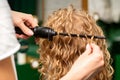 Hands of hairstylist curl wavy hair of young woman using a curling iron for hair curls in the beauty salon rear view. Royalty Free Stock Photo