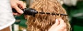 Hands of hairstylist curl wavy hair of young woman using a curling iron for hair curls in the beauty salon rear view. Royalty Free Stock Photo