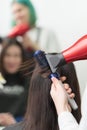 Hands of hairstylist dries brunette hair of client using hair dryer and comb in beauty salon Royalty Free Stock Photo