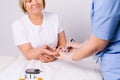 Hands of a healthcare professional using a glucometer to take an analysis from an older woman on a white background.