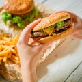 Hands hold american burger and french fries, sauce on wooden plate Royalty Free Stock Photo
