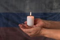 Hands hold a burning candle against the background of the flag of Russia. The concept of mourning and sadness in the