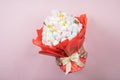 Hands hold edible marshmallow bouquet through torn hole on pink paper background. Bakery advertising concept, recipe