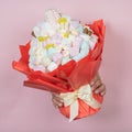 Hands hold edible marshmallow bouquet through torn hole on pink paper background. Bakery advertising concept, recipe