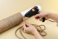 Hands hold electric hot glue gun to make rope around column for scratching post for cats
