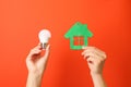 Hands hold energy saving bulb and house on red background Royalty Free Stock Photo