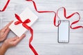 Hands hold Gift Box with red ribbon and smartphone on a woodem background Royalty Free Stock Photo
