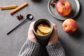Hands hold a gray glass with homemade apple punch or cider with apples and cinnamon on a dark background with fresh fruits and