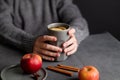 Hands hold a gray glass with homemade apple punch or cider with apples and cinnamon on a dark background with fresh fruits and