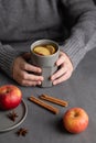 Hands hold a gray glass with homemade apple punch or cider with apples and cinnamon on a dark background with fresh fruits and