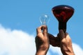 Hands hold infrared lamp and transparent incandescent light bulb against blue sky background