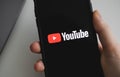 Hands hold the iPhone with Youtube app logo on the screen.