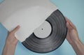 Hands hold an old vinyl record in an old paper case on a light blue background. Royalty Free Stock Photo