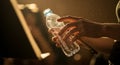 Hands hold a plastic water bottle against a dark background, illuminated by a backlight, creating a dramatic and refreshing image Royalty Free Stock Photo