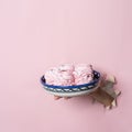 Hands hold a plate with homemade pink marshmallows through a torn hole on a pink paper background. Bakery advertising concept, rec