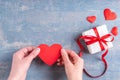 Hands hold a red heart shape next to a gift with a red ribbon bow and red hearts on a wooden blue background Royalty Free Stock Photo