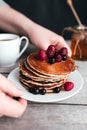 Hands hold white plate with pancakes, berries, honey, coffee cup on wooden table Royalty Free Stock Photo