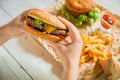 Hands holding american burger and french fries, sauce on wooden plate Royalty Free Stock Photo