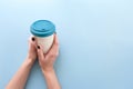 Hands holding bamboo reusable takeaway cup with lid on, on blue background Royalty Free Stock Photo