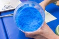 Hands holding beaker of blue chemical, Copper Sulphate Pentahydrate